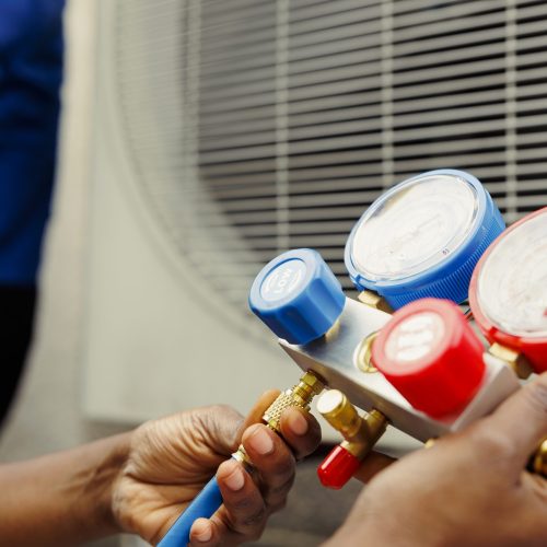 Close up of competent mechanic holding manometers used for checking hvac system refrigerant. Expert repairman using manifold indicators to check high or low freon levels of air conditioner tank